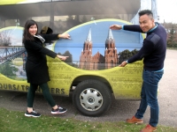 Svečiai iš Londono kinų kilmės Britanijos piliečiai Finola Fionan ir Fion Foo šėlioja šalia anykštėniškais vaizdais išpuošto automobilio, stabtelėjusio aikštelėje prie Siauruko stoties. Mano nuotrauka.